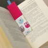 Livre ouvert, marque-page en tissu rose et chouettes avec ruban dépassant du livre, fond en bois