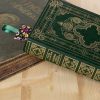 Livre fermé à couverture verte et motifs dorés, marque-page en tissu fleurs avec ruban dépassant du livre, fond en bois