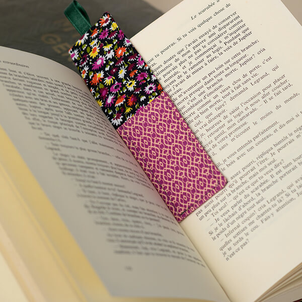 Livre ouvert, marque-page en tissu fleurs et motif graphique avec ruban dépassant du livre, fond en bois