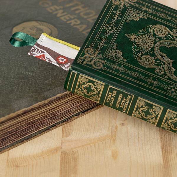 Livre fermé avec une couverture verte à motifs dorés, marque-page en tissu avec ruban dépassant du livre, fond en bois