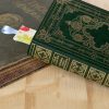 Livre fermé à couverture verte et motifs dorés, marque-page en tissu fleurs avec ruban dépassant du livre, fond en bois